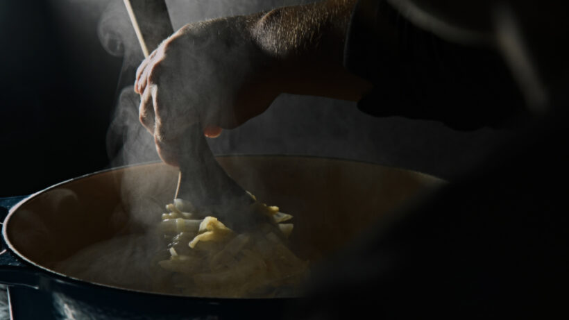 Dark and moody image of sautéing onions with steam curling around the image