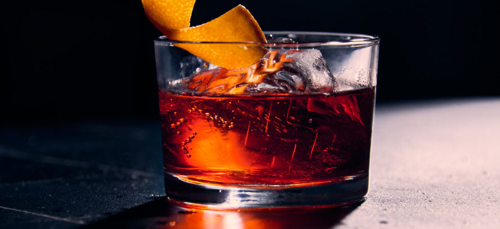 Night Cap Negroni in a glass with a clear ice cube and orange peel garnish