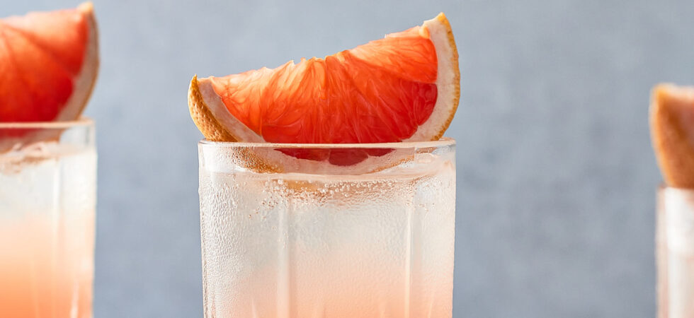 Up-close, grapefruit wedge place on top of a paloma cocktail in a highball glass.