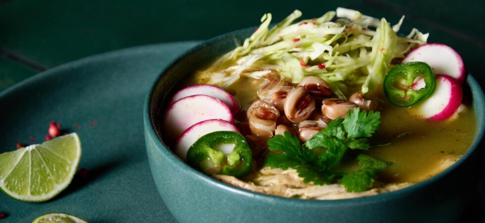 A bowl of pozole verde topped with sliced radishes and jalapeños, shredded cabbage, and cilantro.