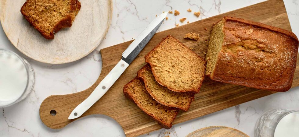 A loaf of banana bread with cut slices that are plated and partially eaten