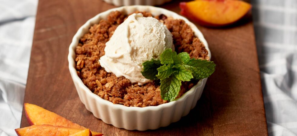 Small nectarine crisp with cinnamon-oat topping in a ramekin with a scoop of ice cream and a sprig of mint.