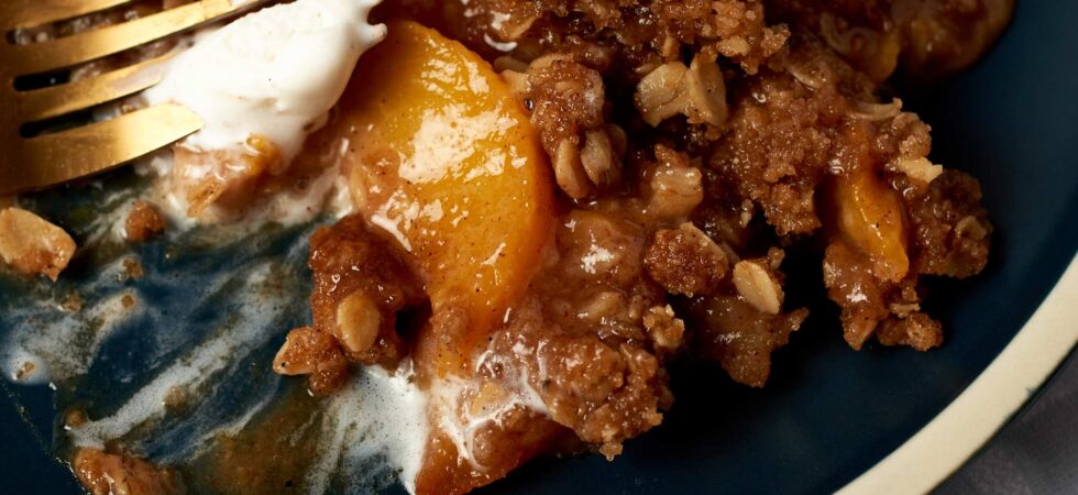 A half-eaten helping of nectarine crisp with cinnamon-oat topping and melted ice cream, on a plate.