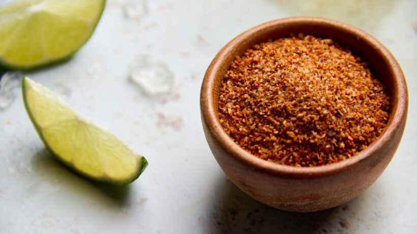 Tajín in a small, wooden pinch bowl next to some sliced lime wedges.