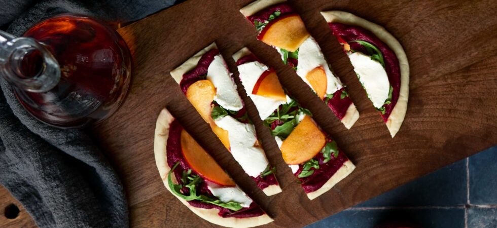 A roasted strawberry, beet, and goat cheese flatbread sliced and ready for a white balsamic drizzle.