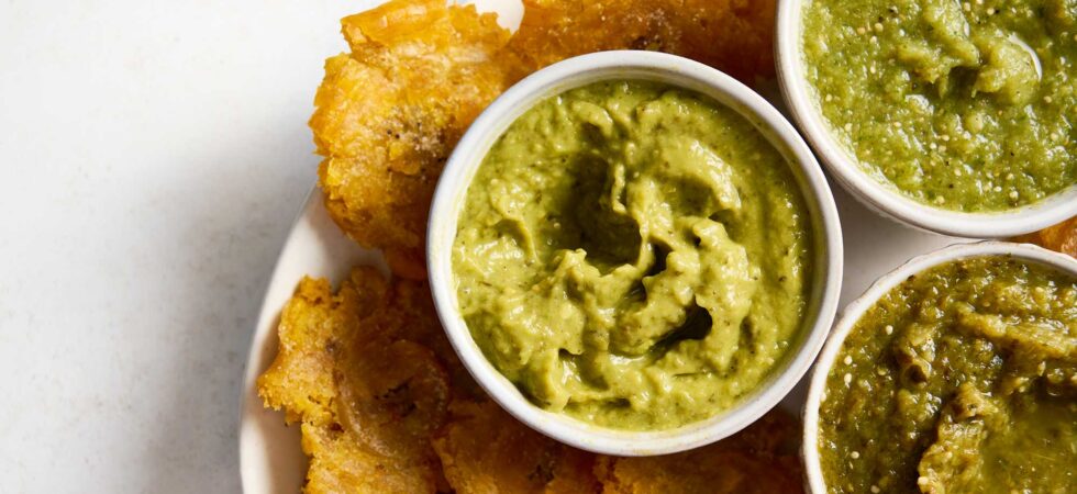 Three different variations of salsa verde, in dip bowls on a plate of tostones.