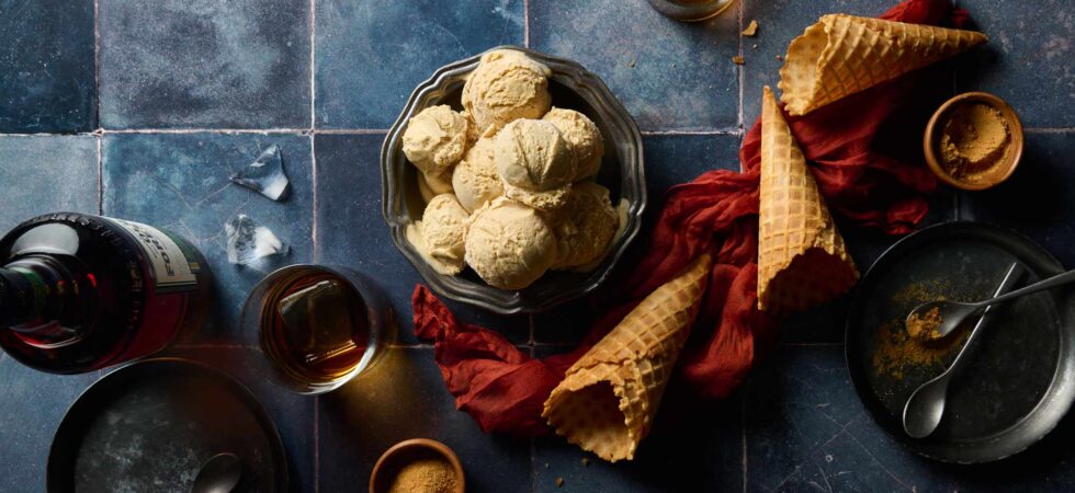 Glasses of bourbon, toasted milk powder, and waffle cones surround a large metal bowl of pre-scooped Browned Butter Bourbon Ice Cream.