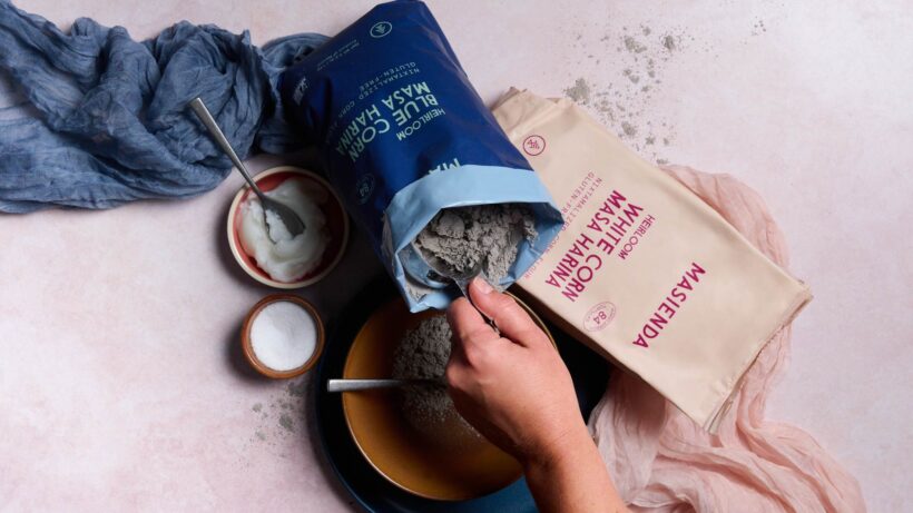 Scooping blue masa harina out of its packaging for corn tortillas. Also shown, white masa harina, salt, and lard in separate bowls.