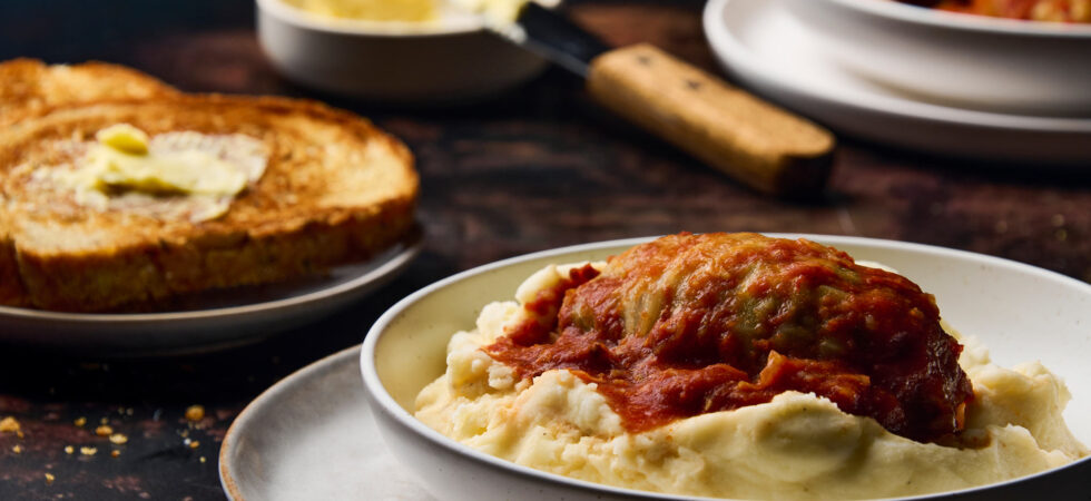 A stuffed cabbage roll plated on a bed of mashed potatoes with toasted, buttered rye bread.