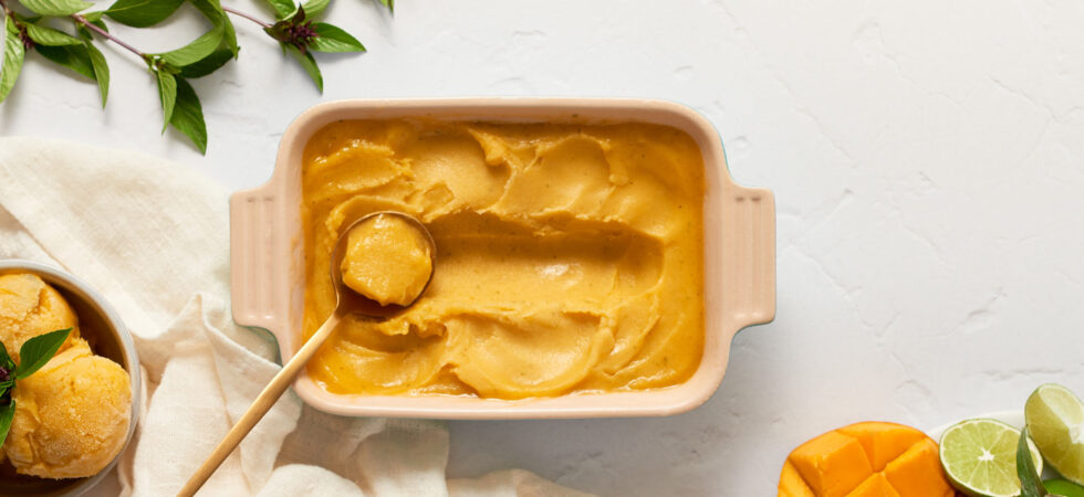 Overhead image of a dish of Mango, Pineapple Tropical Sorbet with a scoop taken out of it.