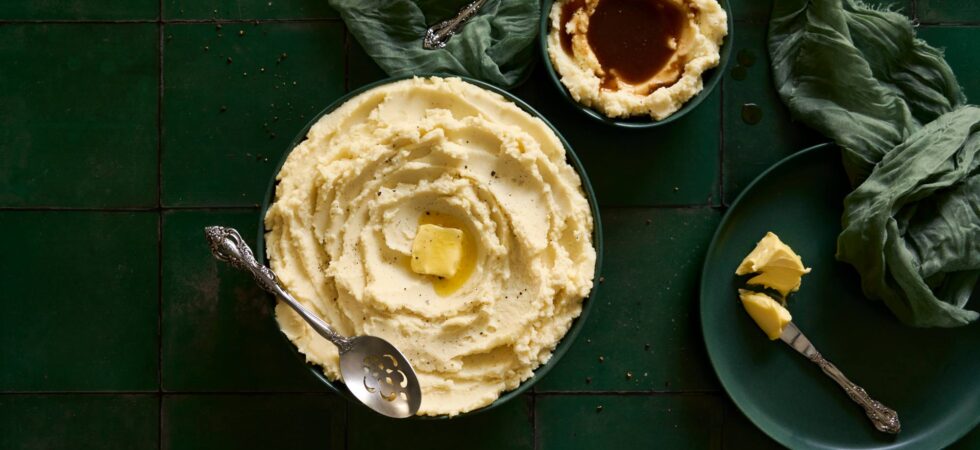 Homestyle mashed potatoes in two bowls: one with a melted pat of butter and the other with gravy.