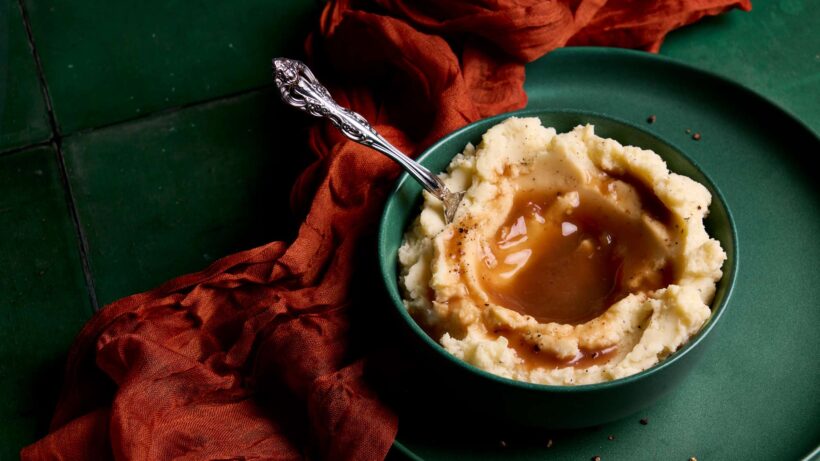 Homestyle mashed potatoes in a bowl with gravy poured into the center.