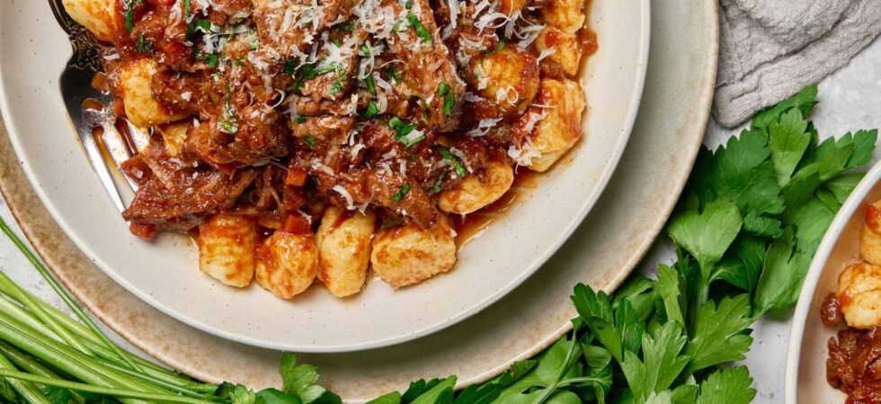 braised beef ragù plated with fresh gnocchi and garnished with grated parmesan and chopped parsley.