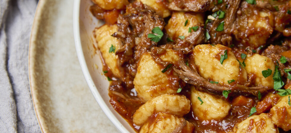 braised beef ragù plated with fresh gnocchi and garnished with chopped parsley.