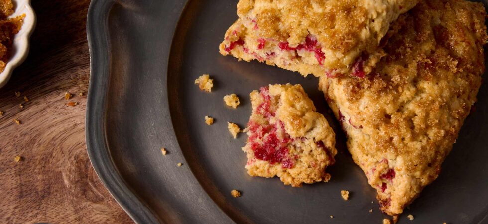 Close up of two cranberry-orange cream scones on a plate with one broken open to reveal the cranberry jam ribbon.