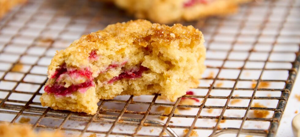 Close up of a cranberry-orange cream scone on a wire cooling rack with a bite taken out of it.