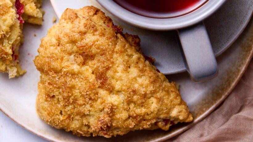 Close up of a cranberry-orange cream scone on a plate with a cup of black tea.