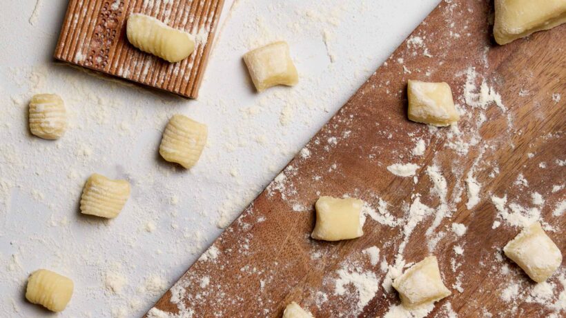 Top-down view of homemade potato gnocchi. Some are unrolled on a cutting board, and some have been rolled down a gnocchi board for their signature ribbed texture.