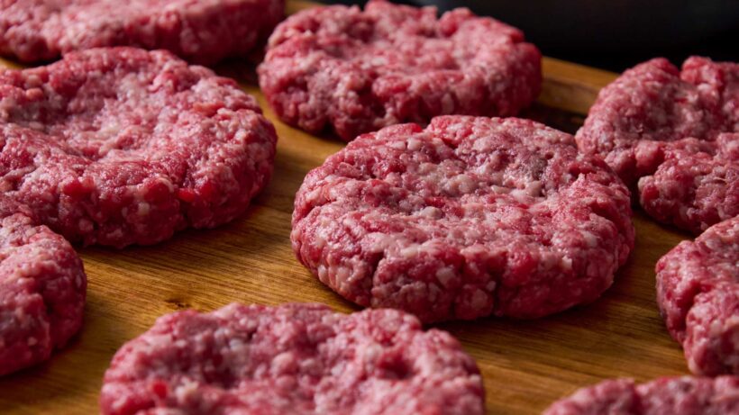 Uncooked burger patties laid out on a wooden cutting board.