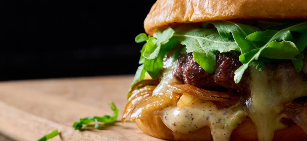 close up of a gourmet griddled onion and brie burger on a wooden cutting board.