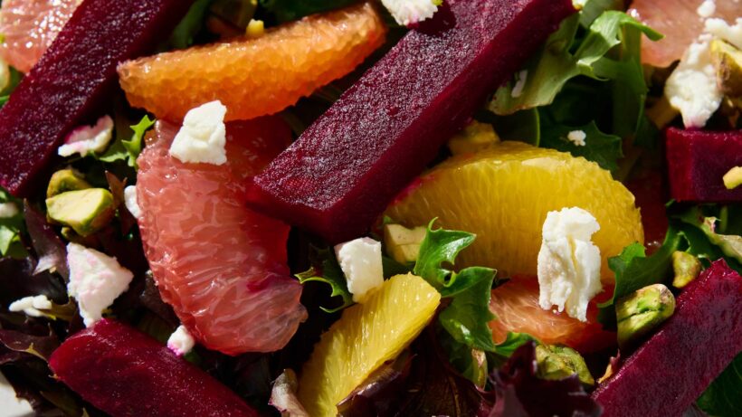 Closeup of a marinated beet and citrus salad with goat cheese crumbles and chopped pistachios.