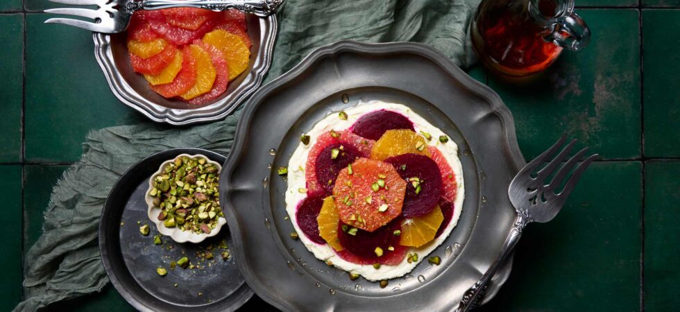 Top down view of a marinated beet and citrus salad, with sliced beets and citrus, on a bed of whipped goat cheese and topped with chopped pistachios.