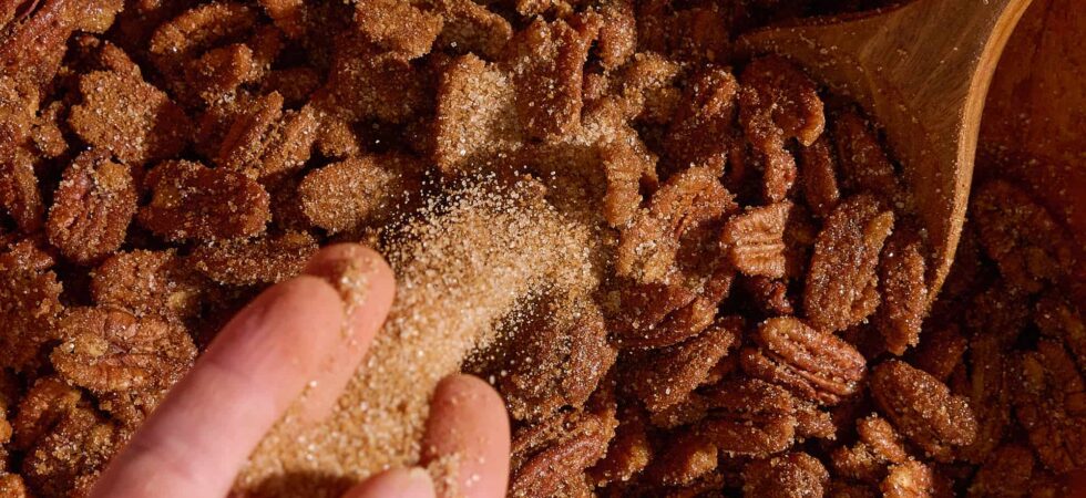 Pouring a cinnamon-sugar mixture onto pecans, to make Cinnamon Roasted Pecans.